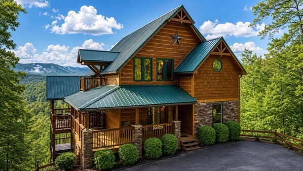 A two-story log cabin with a metal roof, a stone foundation, and a porch with a railing.