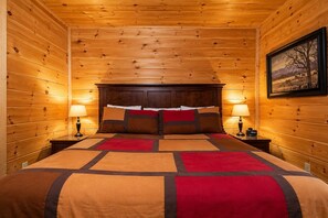 A wooden-paneled room with a bed, two bedside lamps, and a framed picture on the wall.