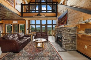 A spacious living area with a stone fireplace, leather sofas, and a large window overlooking a mountainous landscape.