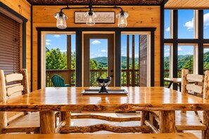 A wooden dining table with chairs, a bowl of fruit, and a sign above the windows.