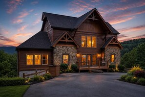 A large, two-story log cabin with stone accents, multiple windows, and a well-maintained driveway.