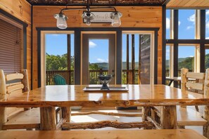 Uma mesa de jantar de madeira com cadeiras, um lustre e vista para o exterior.