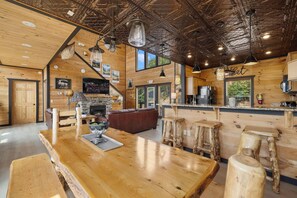 Um interior rústico com uma mesa de jantar de madeira, banquetas de bar, lareira e uma área de cozinha.