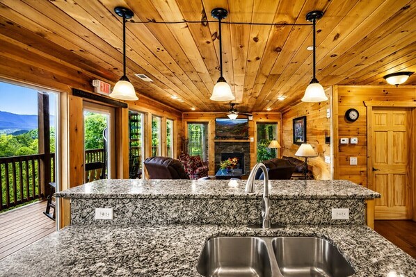 A kitchen with granite countertops, stainless steel sinks, and pendant lighting.