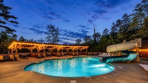 A swimming pool with a slide, lounge chairs, and a covered area with string lights.
