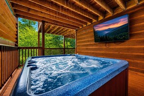A hot tub with a wooden deck and a TV screen displaying a scenic view.