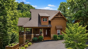 A two-story wooden house with a porch, a small attached garage, and a driveway leading to the entrance.