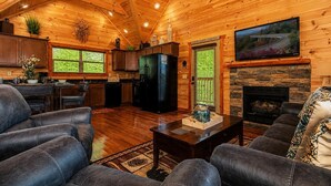 A log cabin interior with a living room, kitchen, and fireplace. - Cabin + FREE Resort Amenities | Pigeon Forge (Pigeon Forge)