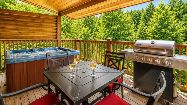 Une terrasse en bois avec un jacuzzi, un barbecue et une table avec des chaises.