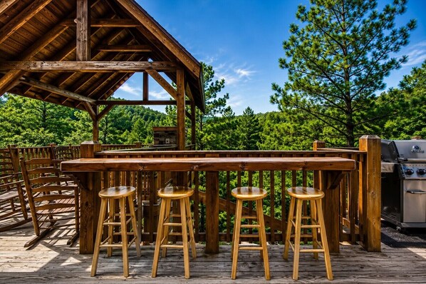 A wooden deck with a barbecue grill and four stools.