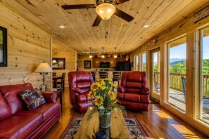 A cozy cabin interior with a wooden ceiling, leather chairs, a sofa, and a dining area. - Luxury Cabin w/ All-Inclusive Resort Amenities (Pigeon Forge)