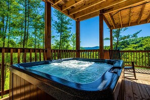 A hot tub on a wooden deck with a view of a forest and mountains. - Luxury Cabin w/ All-Inclusive Resort Amenities (Pigeon Forge)