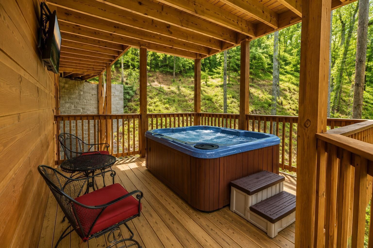 Une terrasse en bois avec un jacuzzi, une table et des chaises, et un mur en pierre.