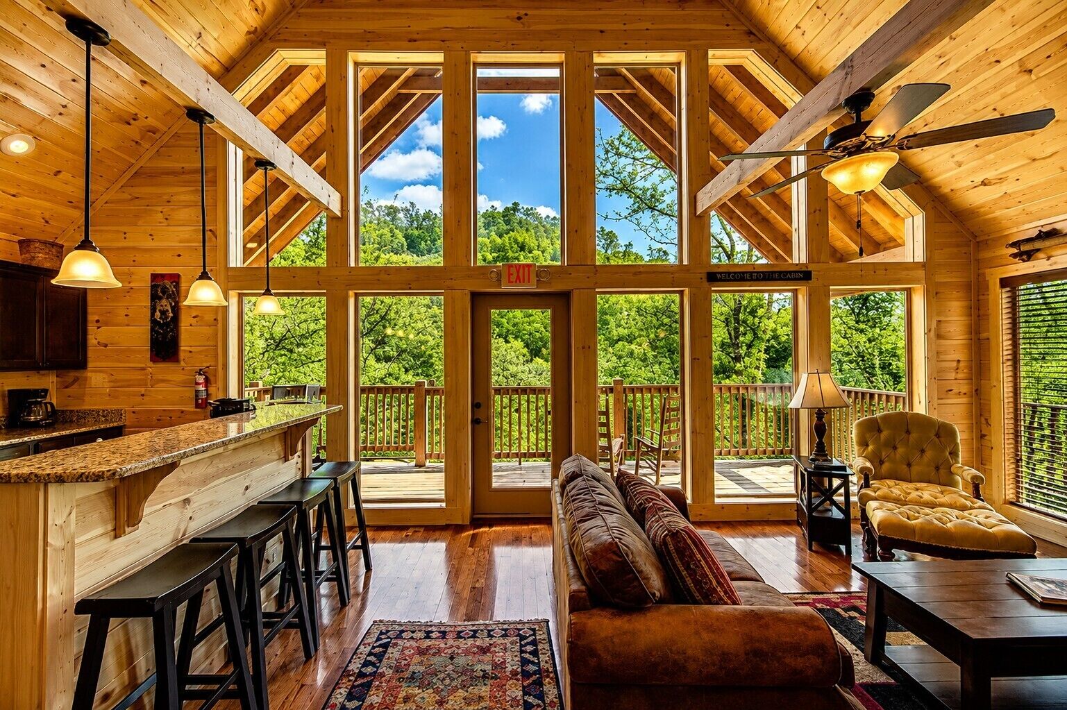 A spacious cabin interior with a large wooden-framed window, a cozy seating area, and a kitchen with a bar.
