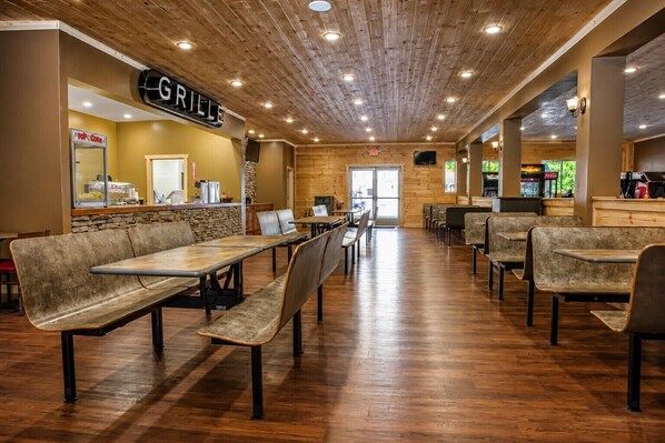 A restaurant with wooden ceiling, tables, and benches, a grill sign, and a counter with a beverage machine. - Cabin + FREE Resort Amenities | Pigeon Forge (Pigeon Forge)