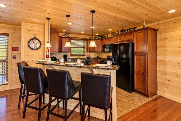 A kitchen with wooden cabinets, a black refrigerator, and a bar area with leather chairs.