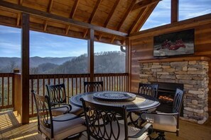 A wooden deck with a stone fireplace and a round table with chairs. - Cabin + FREE Resort Amenities | Pigeon Forge (Pigeon Forge)