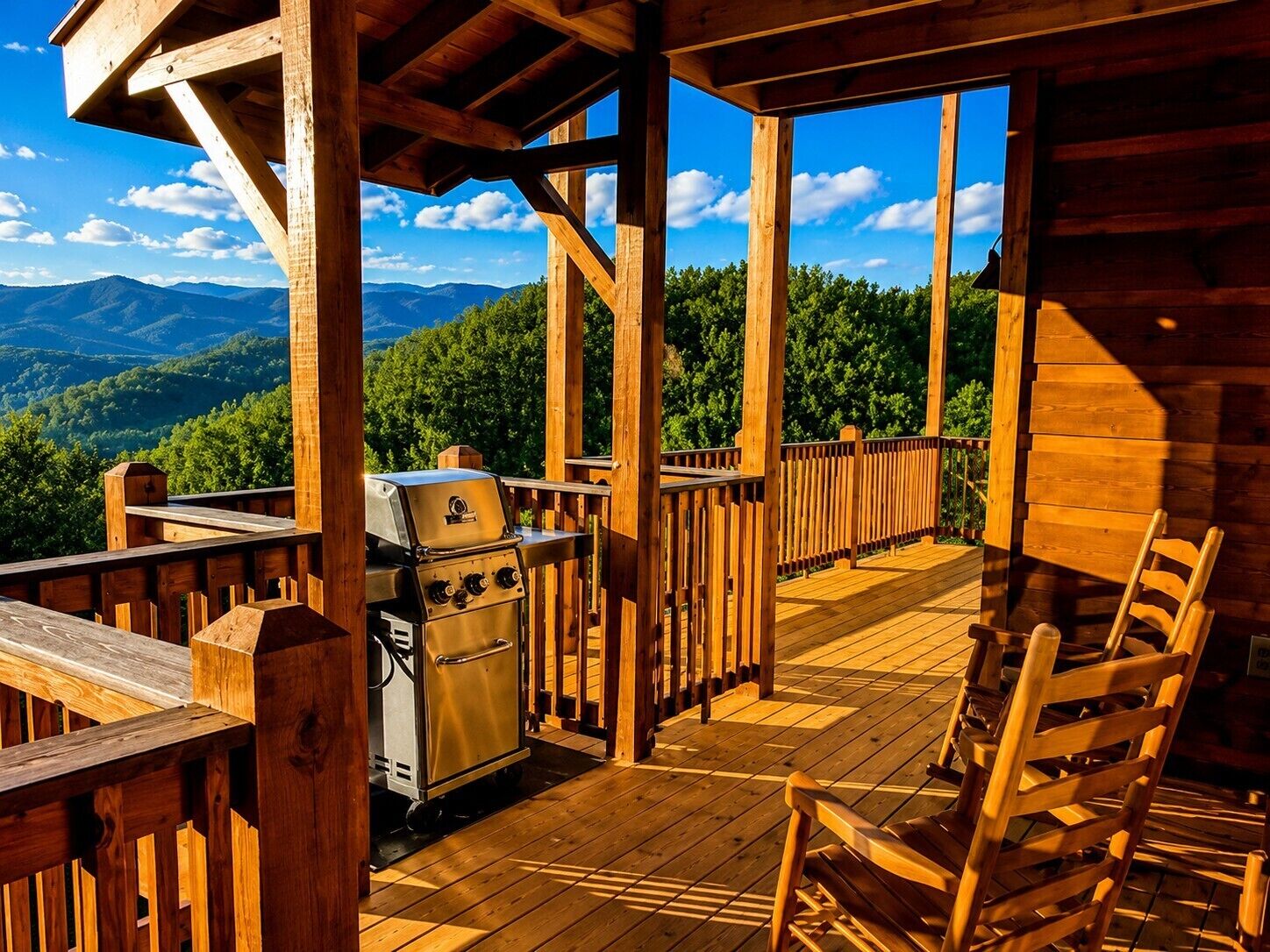 Una terraza de madera con una parrilla y sillas, con vistas a un paisaje montañoso.