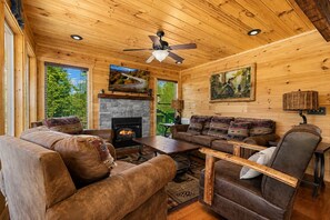 A cozy cabin interior with a fireplace, wooden furniture, and large windows.