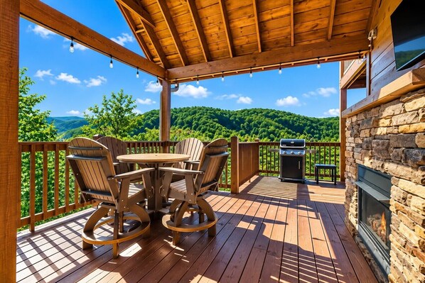 A wooden deck with a table and chairs, a grill, and a stone fireplace.