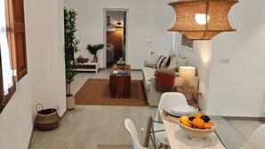A modern dining area with a glass table, white chairs, and a woven pendant light. A dining table set with plates, bowls, and a fruit basket is visible. - Mediterranean home (Palma)