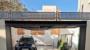 A car parked under a covered driveway with a metal gate and a brick wall in the background. - Mediterranean home (Palma)