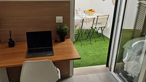 A compact office space with a wooden desk, a laptop, a potted plant, and a white chair. It features a sliding glass door leading to a small outdoor area with a table and chairs. - Mediterranean home (Palma)