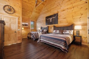 Un dormitorio estilo cabaña de troncos con dos camas, paredes de madera, un ventilador de techo y una gran obra de arte de cabeza de toro.