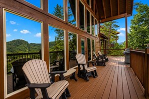 Eine Holzterrasse mit Adirondack-Stühlen und Blick auf eine gebirgige Landschaft.