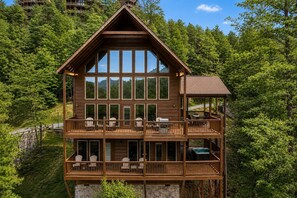 Una cabaña de madera de dos pisos con varios balcones, ventanas amplias y un jacuzzi en la terraza superior.