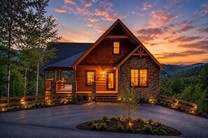 A log cabin with a stone exterior, a porch, and a view of the surrounding forest. - Near Dollywood + Resort Amenities Included (Pigeon Forge)