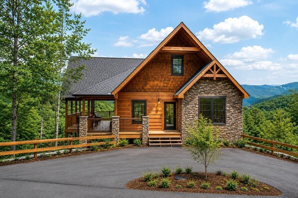 A log cabin with a stone extension, a covered deck, and a view of the surrounding forest. - Near Dollywood + Resort Amenities Included (Pigeon Forge)