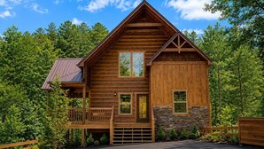A log cabin with a porch, a garage, and a stone foundation. - Cabin + FREE Resort Amenities | Pigeon Forge (Pigeon Forge)