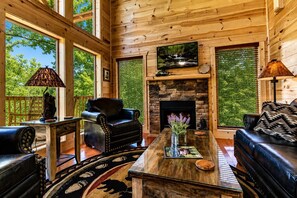 A log cabin interior with a fireplace, leather furniture, and large windows. - Cabin + FREE Resort Amenities | Pigeon Forge (Pigeon Forge)