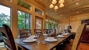 A wooden dining room with a long table set for a meal, large windows, and a ceiling with hanging lights. - Near Dollywood + Resort Amenities Included (Pigeon Forge)