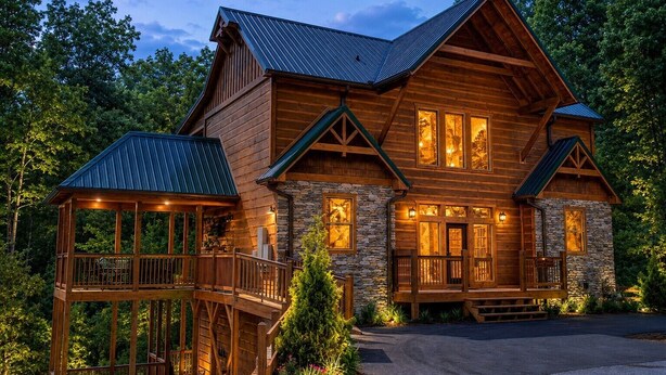 A large log cabin with a stone foundation, multiple windows, and a wooden deck. - Near Dollywood + Resort Amenities Included (Pigeon Forge)