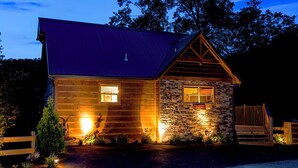 Une cabane rustique en rondins de bois, avec une façade en pierre, un porche en bois et un toit en métal.
