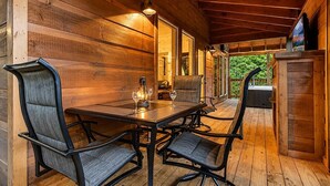 A wooden deck with a table and chairs, a lantern, and a view of greenery. - Near Dollywood + Resort Amenities Included (Pigeon Forge)