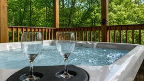 A hot tub with two glasses on a table, surrounded by a wooden deck and trees. - Near Dollywood + Resort Amenities Included (Pigeon Forge)