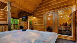 Una cabaña de madera con jacuzzi, televisor y cama con ropa de cama estampada.
