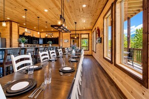 A wooden interior with a dining area set for a meal, kitchen cabinets, and large windows offering a view. - Near Dollywood + Resort Amenities Included (Sevierville)