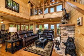 A spacious living area with a fireplace, leather furniture, and a balcony with wooden railings. - Cabin + FREE Resort Amenities | Pigeon Forge (Sevierville)