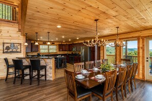 A wooden cabin interior with a dining area, kitchen, and a balcony with a view.