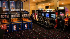 An indoor arcade with basketball and racing game machines, wooden walls, and a patterned floor.