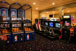 An indoor arcade with basketball and racing game machines, wooden walls, and a patterned floor. - Luxury Cabin w/ All-Inclusive Resort Amenities (Pigeon Forge)