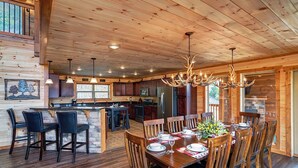 A wooden cabin interior with a dining area, kitchen, and bar. - Luxury Cabin w/ All-Inclusive Resort Amenities (Pigeon Forge)