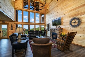 A spacious living room with a fireplace, leather furniture, and a large window offering a scenic view.