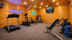 A gym with exercise equipment, a neon sign, and a painting on the wall.