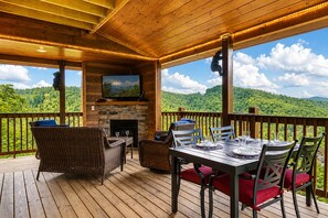 A wooden deck with a stone fireplace, wicker furniture, and a table set for dining. - Near Dollywood + Resort Amenities Included (Sevierville)