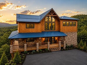 A two-story log cabin with a stone foundation, large windows, and a porch with railings. - Near Dollywood + Resort Amenities Included (Sevierville)